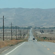 A road stretches to the horizon with mountains in the distance.