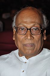 A photograph of an old man wearing white kurta and glasses.