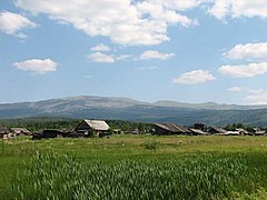 Paysage de montagne, quelques maisons de bois et un massif modéré au loin.