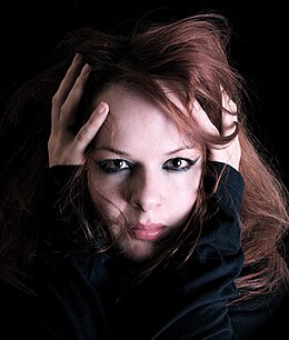 Photographie d'un visage féminin vu de face, avec yeux fardés et abondante chevelure rousse.