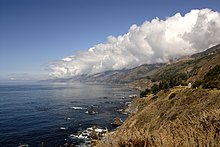 Mountain range along the coast with calm seas and a horizontal cloud formation covering mountain tops