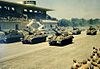 Colour picture of Sherman tanks passing a saluting diaz in an autodrome.