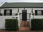 Free-standing single storey vernacular cottage; double pitched corrugated iron roof with gable ends; sash windows (12 panes) and louvred shutters; solid panelled door with fanlight; all possibly original; plastered boundary wall. Type of site: Dwelling, Hotel Current use: House.