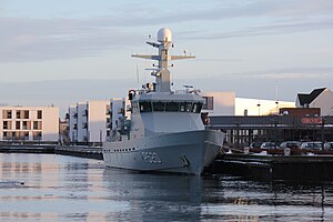 A grey warship docked alongside a wharf