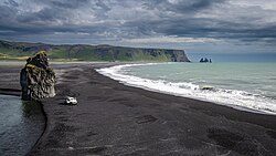 Vue d'Arnardrangur avec en arrière-plan la Reynisfjall et les Reynisdrangar.