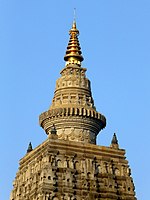 photograph of the pinnacle of the Mahabodhi temple at the top of a truncated pyramid with a gold metal cone-shaped finial at the top, background is a clear blue sky