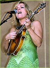 A blonde woman in a green dress singing and playing the mandolin.