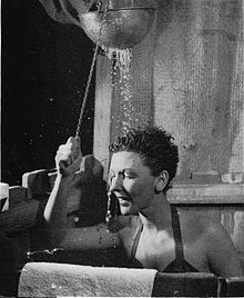 Martin, wearing a swimsuit, stands in an improvised shower stall as water pours down on her.