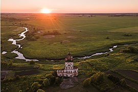 Photographie d'une plaine plate avec une rivière et un clocher d'église, sur fond de soleil couchant.