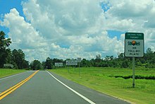 A road with a sign with text "Orchard Pond Parkway: SunPass or toll-by-plate"