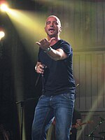 A man wearing jeans and a leather jacket appears on stage