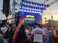 Concert Venue in Tel Aviv Israel with Pride Flags. One person is wearing a trans flag as a cape with the Star of David in the center