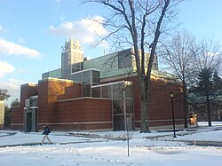 A glass and brick building rests behind a leafless tree on a snowy day