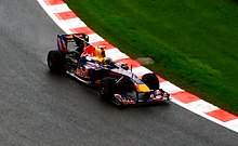 A navy blue Formula One car being driven at speed on a dry race track