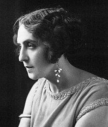 A white woman in near-profile, with wavy cropped hair, wearing beaded drop earrings.