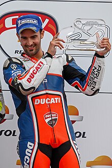Smiling rider wearing a leather suit holding a trophy aloft