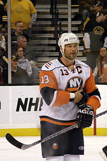 An ice hockey player on the ice. He is wearing a white jersey with orange and blue trim.