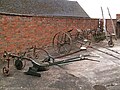 Display of farm machinery in the yard: single furrow plough, potato plough, and rakes.