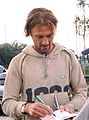 Unshaven white man with scruffy hair wearing a casual hooded top signs autographs