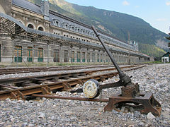 Vue d’un aiguillage en premier plan, avec une gare ferroviaire en arrière plan.