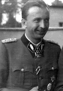 Black-and-white photograph of a smiling man in semi profile wearing a military uniform and an Iron Cross at his neck.
