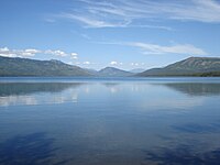 A blue lake with three mountains in the background and a mostly clear sky