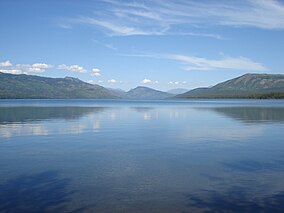 A blue lake with three mountains in the background and a mostly clear sky