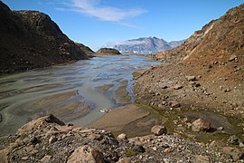 Photographie en couleurs de glaces fondues traversant une vallée, une montagne visible en arrière-plan.