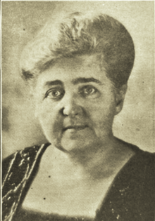 B&W portrait photo of a middle-aged woman with her hair in an up-do, wearing a dark blouse with a square neckline.