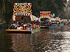 Plusieurs trajineras, embarcations à fond plat typiques, à la suite sur un canal de Xochimilco.