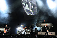 Four musicians perform on a brightly lit stage.