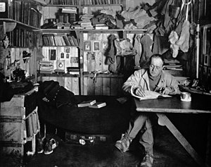 רוברט פלקון סקוט יושב ליד שולחן במגוריו, כותב ביומנו, במהלך משלחת טרה נובה לאנטארקטיקה, שנת 1911 - תצלום מאת הרברט פונטינג.