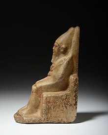 Light brown statuette of a man seated on a throne with high rounded crown, hieroglyphs inscribe on his right on side.