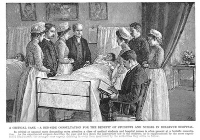 Elderly white man in dark suit surrounded by four nurses and three medical students at bedside of a sick child.