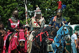 Trois individus en gros plan habillés en armure du Moyen Âge et assis sur des chevaux