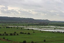 Water on grassy lowland with hills in the distance.