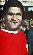 A young black man smiles during a starting lineup. He is wearing a red shirt with a white collar.