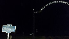 a picture of the marker, in the dark, with a cemetery sign behind it