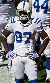 A dark-skinned man wearing a white football jersey and helmet