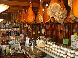 interior of a French food shop, with sausages and hams hanging from ceiling hooks, and jars of charcuterie products on shelves