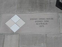 Four square tiles embedded in the facade, arranged in a diamond pattern with the top and bottom tiles lighter in color than the right and left tiles