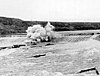 A dynamite explosion tears apart a portion of a weir dam on a river.
