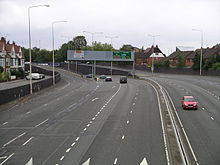 View of the anticlockwise lanes and exit slip roads, with overhead signage visible the road passing underneath the junction 5 roundabout in the distance