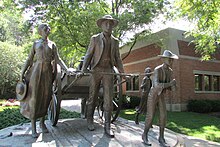 Outdoor statue of a man pulling a handcart, with family members on foot around the cart