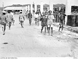 Indigenous peoples carrying Japanese rifles walking along a street in Brunei on their return to their villages on 17 June 1945