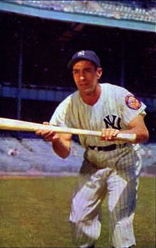 A man in a white baseball jersey with navy blue pinstripes and cap