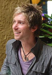 A 34-year-old man with spiky blonde hair, smiling at something to the left of the camera.