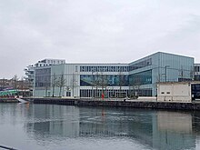 Une photo de face du bâtiment de la bibliothèque Alexis de Tocqueville (Caen), au premier plan un bras d'eau se jetant dans l'Orne.