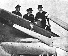Three men stand next to a fighter aircraft and look at it.