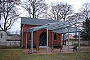 Teile der Friedhofsanlage: Kapelle mit Gruft der Familie Kettlitz (heute Friedhofskapelle), Leichenhalle, straßenseitige Friedhofsmauer einschließlich Einfahrtstor sowie Ziegelpflasterung des Straßenabschnitts vor dem Friedhof und der Zufahrt